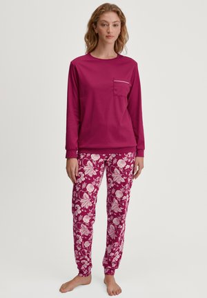 Langärmliges magentafarbenes Oberteil mit einer Brusttasche und weißen Akzenten, kombiniert mit floral gemusterten magentafarbenen und weißen Hosen aus weichem Stoff.