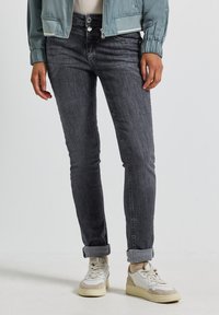 Jean slim-fit en denim gris foncé avec décoloration et ourlets roulés. Portés avec des baskets blanches et beiges. Le matériau semble doux avec une texture lisse.