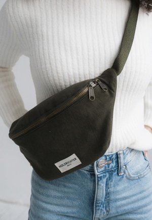 Olivenfarbenes Canvas-Bauchtasche mit einem Reißverschluss oben, ausgestattet mit metallischen Reißverschlusslaschen und einem weißen Etikett mit dem Text "HOLZRICHTER". Verstellbarer Riemen.