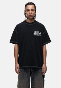 T-shirt noir oversize en coton, présentant des accents blanc cousus et un imprimé graphique portant la mention "GOOD NOTHING" sur la poitrine.