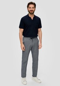 Polo de manga corta en color navy con un bolsillo, combinado con pantalones cuadros en tonos gris y blanco y zapatillas blancas. Outfit casual con un corte moderno.