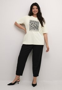 Cream short-sleeve t-shirt with a black abstract graphic, paired with relaxed black trousers, and black slingback heels. Smooth fabric texture.