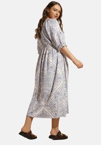 Sininen ja valkoinen kuvioitu maksimekko, jossa on lyhyet puffihihat, joustava vyötärö ja lennokas hame. Yhdistetty tummanruskeisiin tasapohjaisiin sandaaleihin.