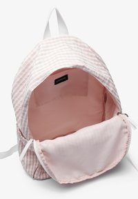 Sac à dos en tissu rayé rose avec des accents blancs. L'intérieur comprend une doublure rose clair et une poche zippée pour le rangement.