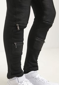 Svarta joggerbyxor med ribbad textur, med flera dragkedjefickor och detaljer. Kombineras med vita högra sneakers.