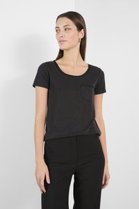 Černé tričko s crew neck výstřihem vyrobené z měkké látky, s krátkými rukávy a náprsní kapsou. Tričko je kombinováno s černými kalhotami.