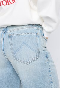 Light blue denim jeans featuring a high-rise fit, standard back pockets, and a subtle textured weave. Accented with visible stitching details.