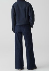 Marinblå kort jacka med en strukturerad design, iklädd vida mörka denimjeans. Slät textur och minimala detaljer, med bakfickor.