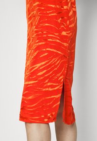 Vestuário vermelho com um padrão de riscas de zebra texturizado. O tecido é leve, com uma fenda lateral e um acabamento suave.
