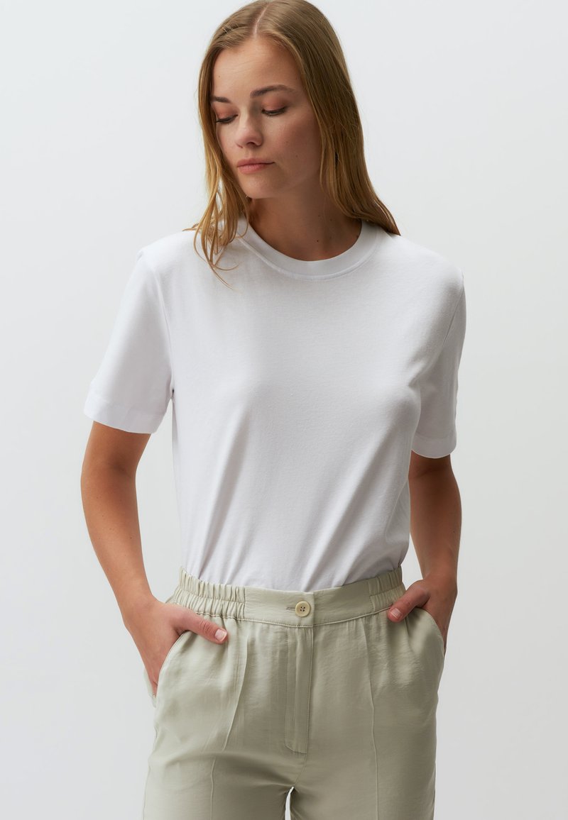 Weißes Baumwoll-T-Shirt mit Rundhalsausschnitt und kurzen Ärmeln, kombiniert mit hellgrünen, elastischen Bundhosen mit Knopfdetails.