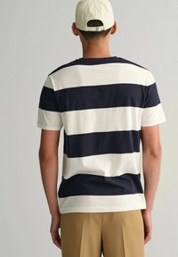 Marineblauwe en witte gestreepte katoenen t-shirt met korte mouwen, met een ronde hals en een relaxte pasvorm, gedragen met beige broeken en een lichte pet.