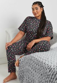 Conjunto de pijama negro con mangas cortas y estampado de estrellas en rosa y blanco. Tela suave y diseño ajustado, acompañado de una manta gris acogedora.