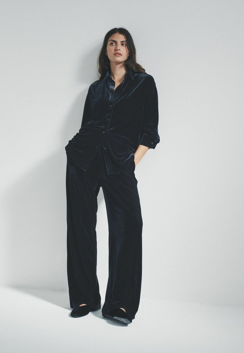 Samt-Pyjama-Set in Dunkelblau, bestehend aus einem Hemd mit Knopfleiste und Kragen sowie lockeren Hosen. Weicher Stoff und eleganter Fall.