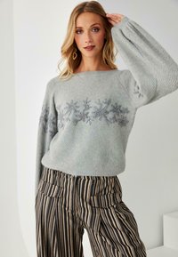Suéter gris claro con bordados florales en el pecho, con mangas globo sueltas. Combinado con pantalones de talle alto a rayas.