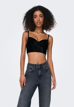 Crop top in velluto nero con scollatura a cuore e spalline sottili, abbinato a jeans scuri grigi a vita alta. Texture liscia e design aderente.