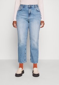 Vaqueros de denim de cintura alta, de color azul claro, con un corte relajado, que cuentan con cinco bolsillos, trabillas para cinturón y un ligero desvanecimiento. Combinados con mocasines beige.