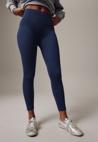 Marineblå ribbede leggings med høj talje, kombineret med sølvfarvede sportssko. Leggingsene er tætsiddende med en glat tekstur.