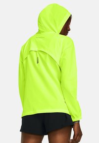 Giacca gialla neon con cappuccio, materiale leggero, con dettaglio di ventilazione sul retro e accenti neri. Maniche lunghe e polsini elastici.