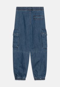 Jeans hlače v temno modri barvi z elastičnim pasom, nabranimi manšetami in dvema stranskima žepoma s pokrovčkom za dodatno funkcionalnost.