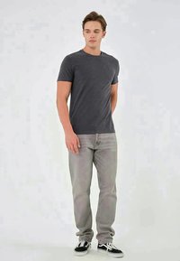Gray cotton t-shirt with short sleeves, paired with light gray jeans and black sneakers. The fit is casual and relaxed.