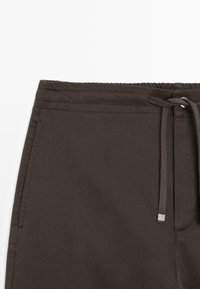 Ciemnobrązowe spodnie z elastycznym pasem, sznurkiem ze srebrnym akcentem, teksturowaną tkaniną i przeszyciami.