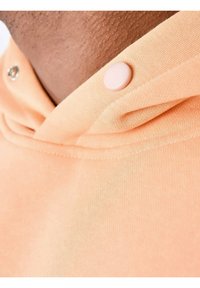 Sudadera de color durazno con una suave textura de algodón, que presenta un cuello doblado y un botón rosa redondo cerca del escote.