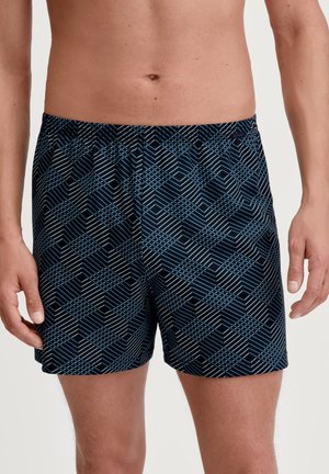 Pantaloni da bagno neri con un motivo geometrico in blu e bianco. Dotati di una vita elastica e di una vestibilità comoda. Realizzati in materiale leggero.