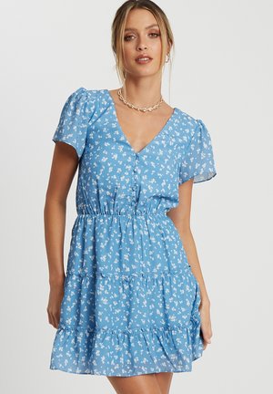 Blue floral dress features short puff sleeves, a V-neckline, and an elastic waist. The tiered skirt has a lightweight, flowing design.