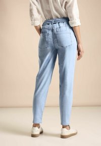 Pantalones elásticos de cintura baja en azul claro con pierna ajustada, que presentan dos bolsillos traseros y una sutil textura de lavado. Las zapatillas blancas complementan el conjunto.
