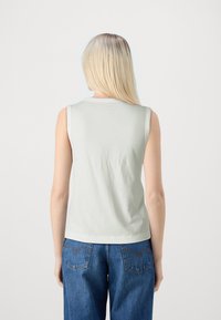 Top sin mangas de color verde claro con cuello redondo, hecho de suave algodón, combinado con jeans de denim azul de cintura alta con bolsillos traseros.