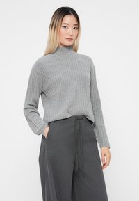 Grauer gerippter Rollkragensweater mit langen Ärmeln, kombiniert mit dunkelgrauen weit geschnittenen Hosen mit gebundenem Bund. Glatte Textur, lässiger Schnitt.