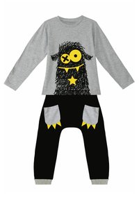 Graues Langarmshirt mit einem schwarzen Monster-Graphic und gelben Akzenten, kombiniert mit schwarzen Hosen mit grauen Taschen und gelben Details.
