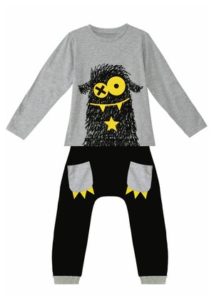 Chemise grise à manches longues avec un graphique de monstre noir et des accents jaunes, associée à un pantalon noir avec des poches grises et des détails jaunes.
