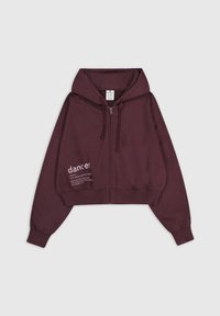 Felpa corta con zip di colore bordeaux in tessuto morbido, caratterizzata da un cappuccio a doppio strato e un dettaglio testuale sul lato sinistro anteriore.