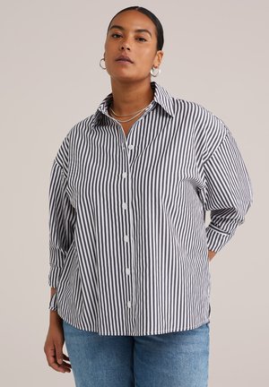 Camisa de botones a rayas en blanco y negro, con cuello, mangas largas y un corte relajado. Tejido suave con detalles de costura visibles.