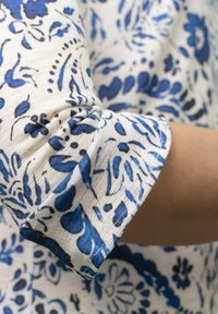 Tela blanca con patrones florales y acentos azules. La tela tiene un acabado texturizado. El puño está enrollado, mostrando claramente el diseño.