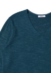 Morska zielona sweter w serek wykonany z teksturowanej dzianiny. Prezentuje subtelne różnice w kolorze i wzorze, z metką z nazwą "CECiL."