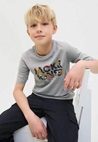 Šedé tričko s krátkým rukávem se barevným grafickým designem "JACK & JONES" na přední straně, doplněné tmavými cargo kalhotami.