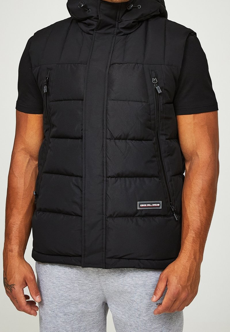 Svart vadderad väst med huva, utrustad med fickor med dragkedja och en logotypapplikation. Tillverkad av texturerat tyg, med en kortad design och utan ärmar.