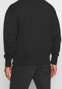 Czarna bluza z okrągłym dekoltem, z prążkowanym wykończeniem na dole i mankietach, wykonana z miękkiego materiału. Widok z tyłu ukazuje prosty design, bez logo i widocznych wzorów.