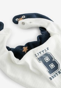 Mörkblå och vit ribbad babyhaklapp med tryckknappar, med en gul stjärndetalj och texten "LITTLE BROTHER" med ett fetstilt 'B'.