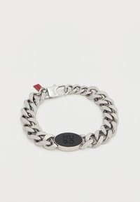 Βραχιόλι αλυσίδας από μέταλλο με μεγάλα συνδεδεμένα κρίκους, γυαλιστερό ασημένιο φινίρισμα, οβάλ μαύρη διακόσμηση λογότυπου και ασφαλές κούμπωμα.