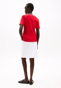 Raudona trumpa rankovė, laisvo kirpimo, derinama su balta sijonu. Juodi butai užbaigia įvaizdį. Medžiaga atrodo lygi ir kasdieniška.