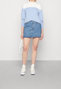 Ljust blå tröja med vita detaljer, jeanstygs kjol och vita sneakers. Liten crossover-väska med rutigt mönster. Enkelt design.