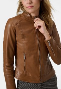 Veste en cuir marron avec un design ajusté, col haut, fermeture éclair à l'avant et deux poches zippées. Présente des accents de couture subtils.