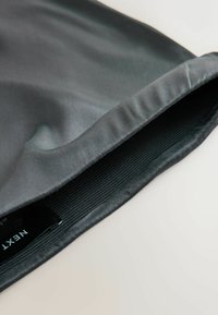 Grauer Satin-Stoff mit glatter Textur, mit einer gerafften Kante und einem elastischen Band, das ein Etikett mit der Marke 'NEXT' zeigt.