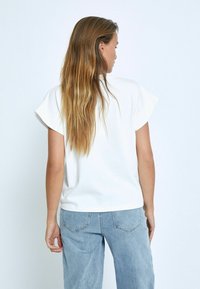 Top blanco de manga corta con un ajuste relajado, que presenta un cuello redondo y un tejido suave y liso. Combinado con pantalones vaqueros de denim azul claro.