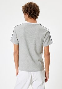Grå kortærmet t-shirt med ribbet tekstur, der har sorte striber langs skuldrene og en hvid krave.