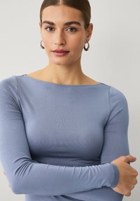 Top azul de manga larga con escote barco, hecho de una tela suave, con un diseño ajustado y una textura lisa. Estilo simple y minimalista.