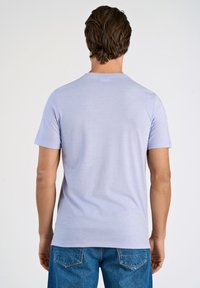 Ljust lila åtsittande t-shirt med korta ärmar och rundad halsringning, tillverkad av ett mjukt och glatt material. Blå denimjeans bärs.